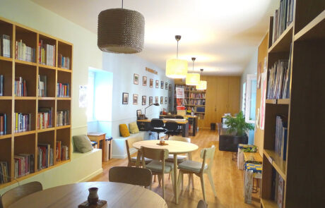 Sala com mesas e cadeiras e várias estantes com livros