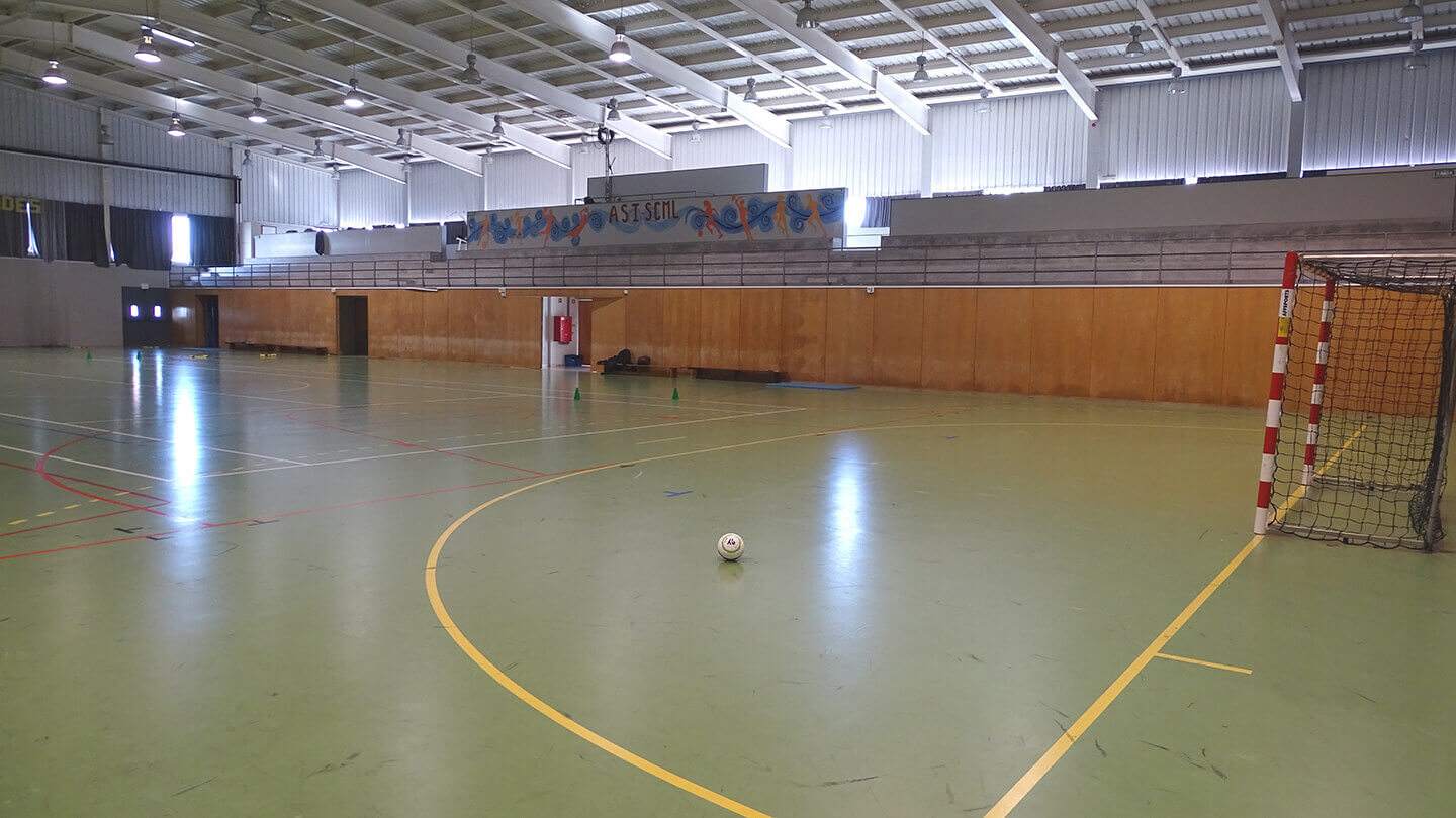 Interior do pavilhão onde se veem as bancadas, uma das balizas e uma bola no meio do campo